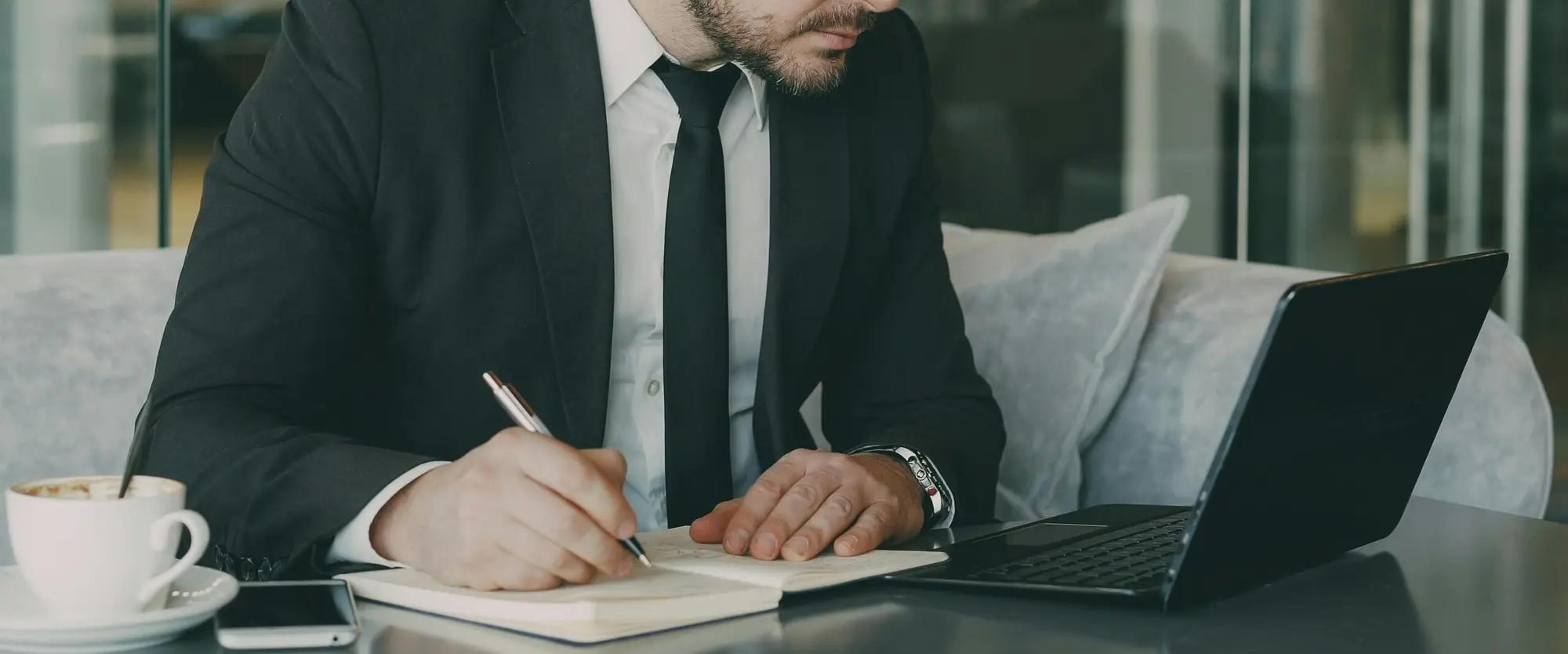 Businessman writing in a notebook beside a laptop