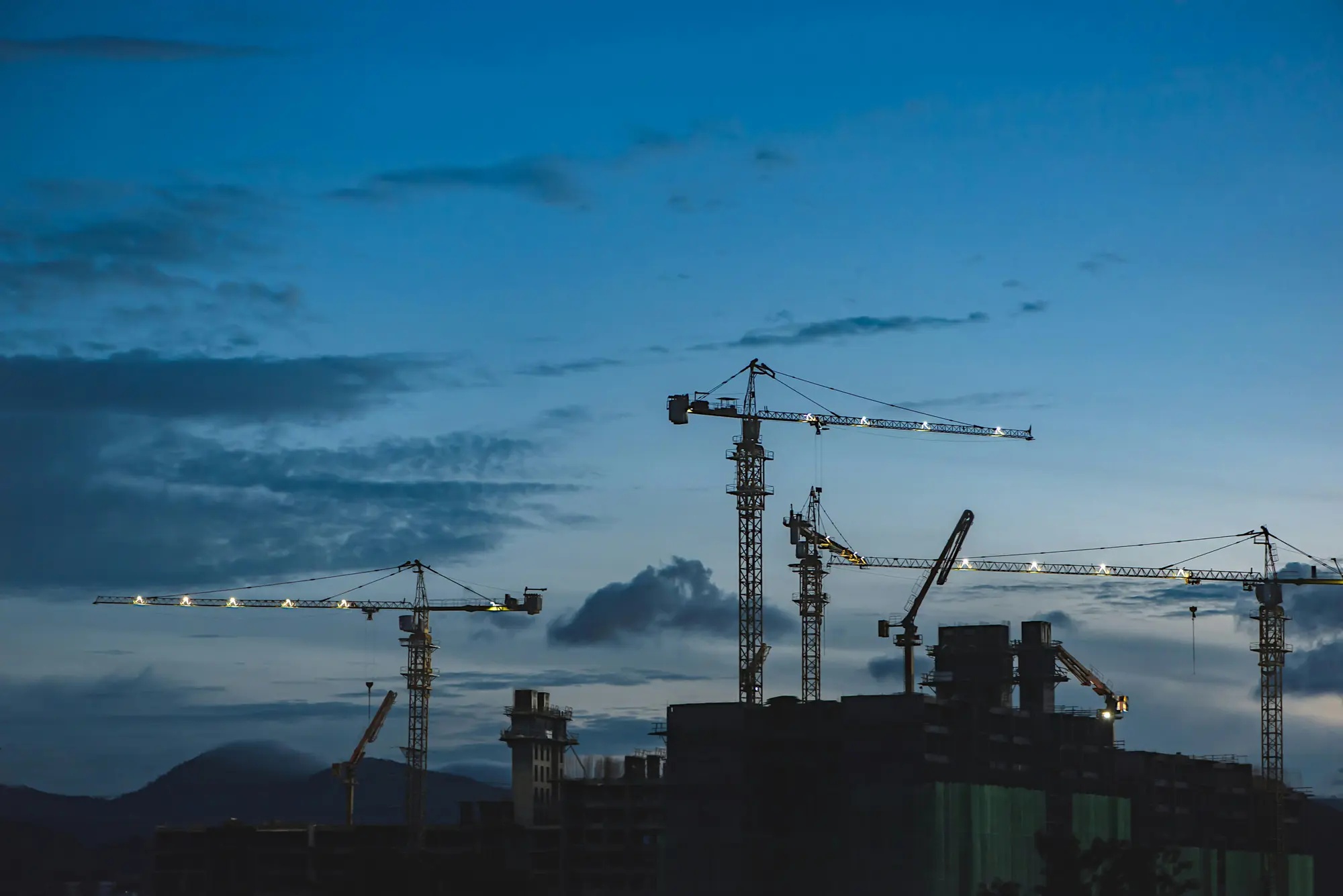 Tower cranes over a commercial construction site at dusk