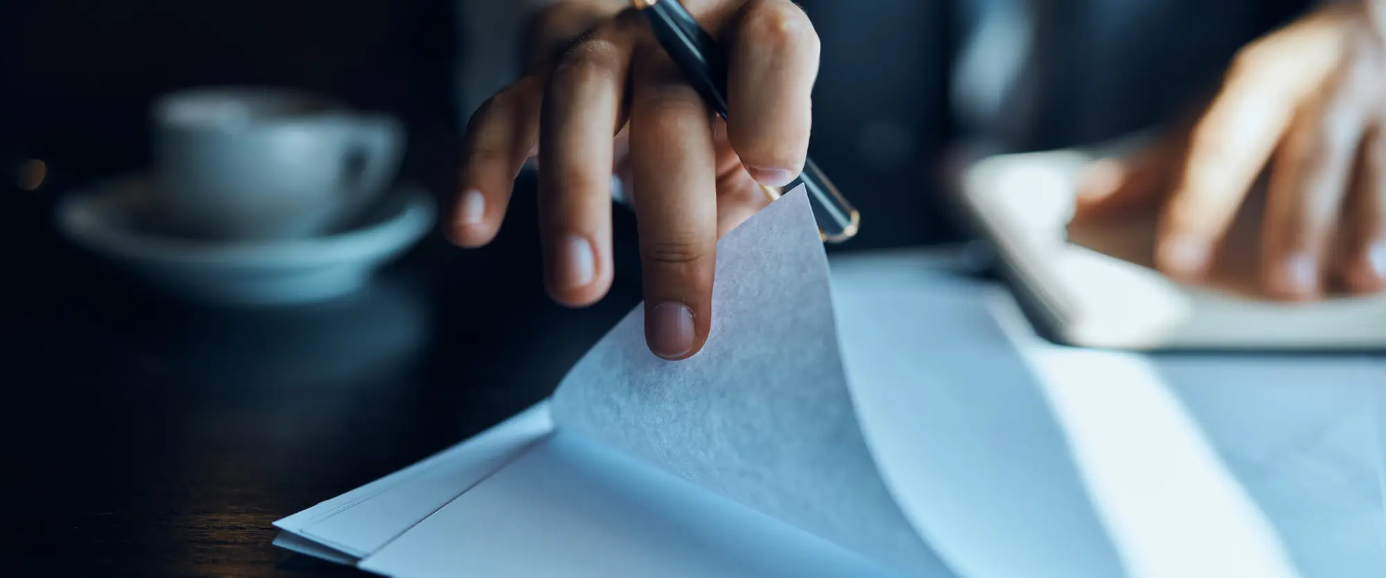 Hand holding a pen while turning the pages of a contract